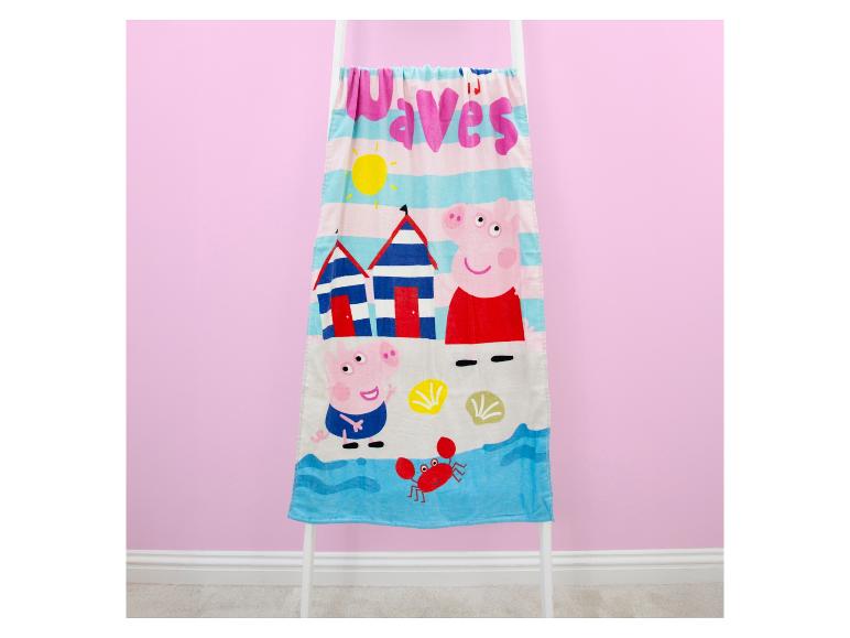 Serviette de plage pour enfants avec cochons de dessin animé, cabines de plage, soleil et crabe sur fond rose.