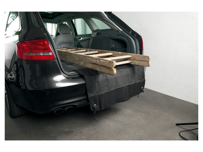 Une échelle en bois dans le coffre d'une voiture, protégée par un protège-pare-chocs noir.