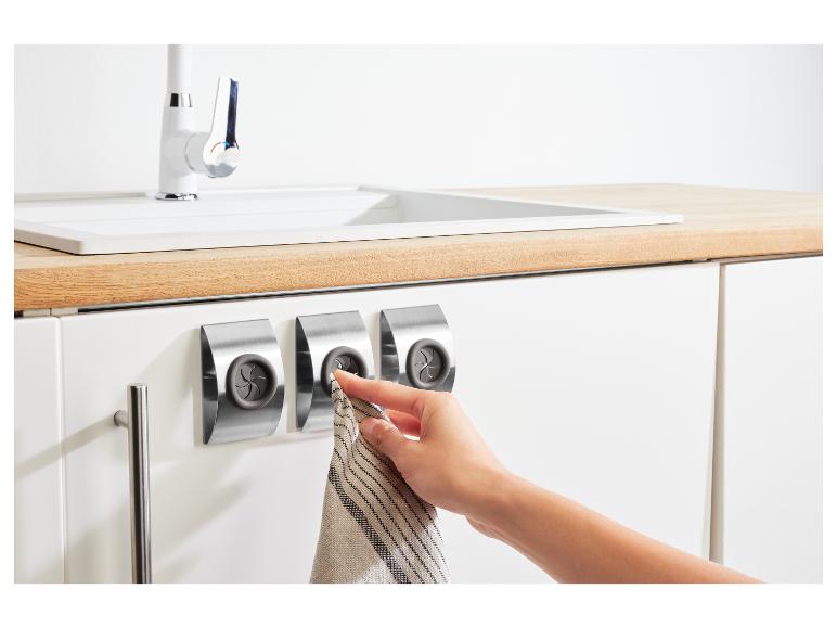Des torchons accrochés à des crochets magnétiques sur un placard de cuisine blanc.