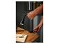 Une main fixe une lampe de bureau noire à bras flexible sur une table en bois.