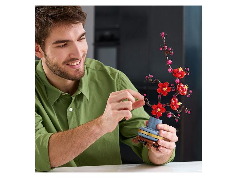 Un homme souriant assemble un bonsaï de fleurs de cerisier en briques de construction.