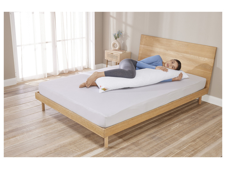 Une femme allongée sur un lit avec un long coussin Serene.
