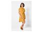 Une femme portant une robe chemise jaune et des mules en daim marron.