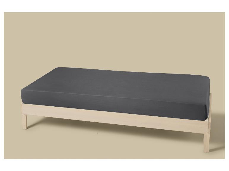 Drap gris sur un lit en bois clair sur fond beige.