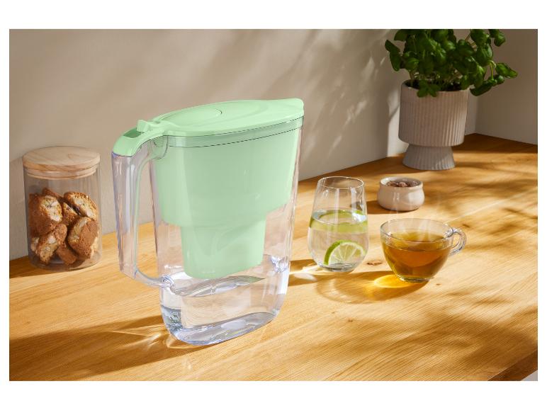 Carafe filtrante à eau vert menthe sur une table en bois, avec des verres et du thé.