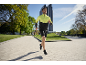 Homme en veste de course jaune et noire et short noir faisant du jogging en extérieur.
