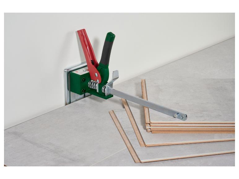 Outil de pose de stratifié avec poignées rouges et vertes, sur un sol stratifié.