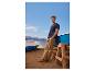 Homme en t-shirt bleu marine et pantalon beige sur la plage, appuyé contre un bateau.