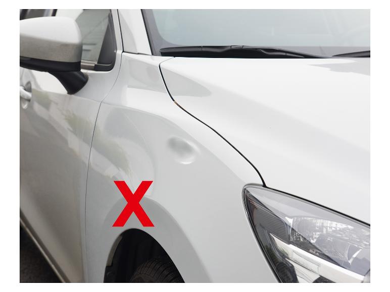 Voiture blanche avec une bosse sur l'aile et un X rouge.