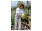 Femme dans une serre tenant une herbe en pot, avec d'autres plantes et fournitures de jardinage.