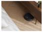 Robot aspirateur noir nettoyant un parquet sous un meuble en bois.
