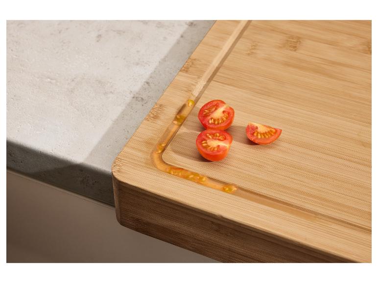 Planche à découper en bambou avec des tomates cerises coupées sur un comptoir de cuisine.
