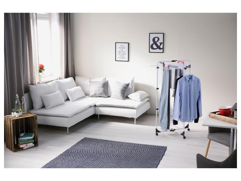 Séchoir à linge avec chemises et pantalons dans un salon moderne avec canapé blanc et tapis.