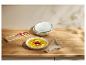 Soupe de potiron garnie, assiettes blanches empilées et serviette sur une table en bois.