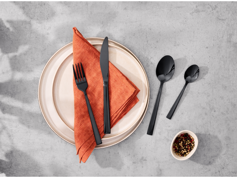 Couverts noirs sur une assiette avec une serviette orange.