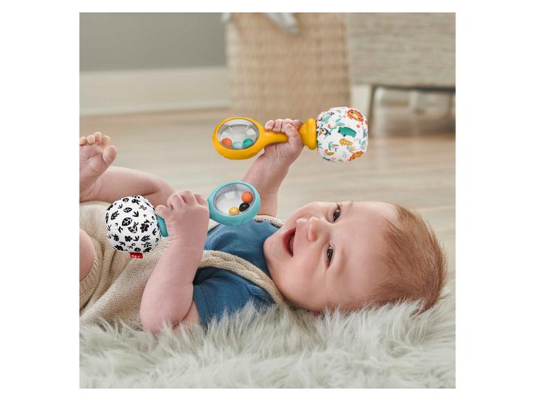 Bébé joyeux jouant avec deux hochets Fisher-Price sur un tapis moelleux.