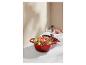 Cocotte en fonte rouge avec un plat cuisiné, des épices et un couvercle sur une surface en marbre.