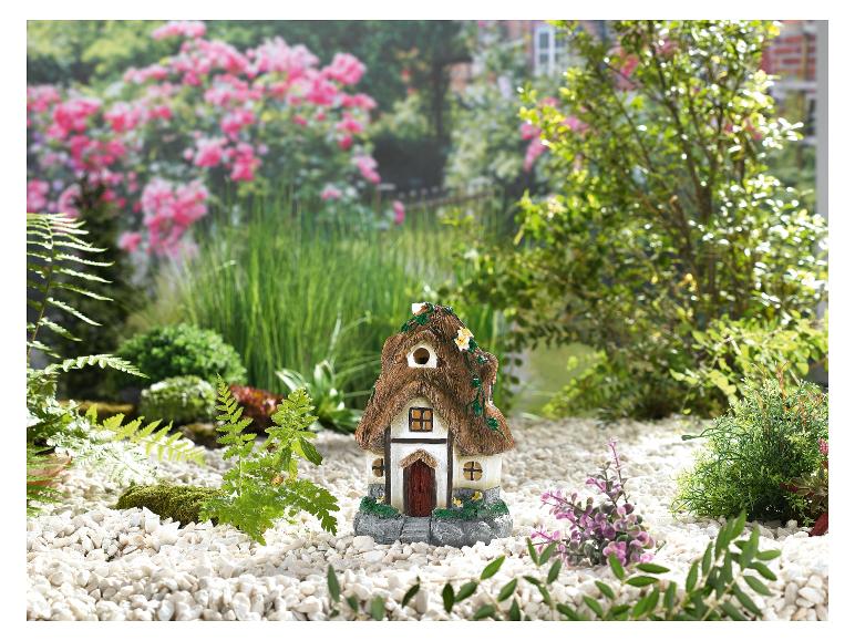 Une petite maison blanche avec un toit de chaume dans un jardin avec du gravier blanc.