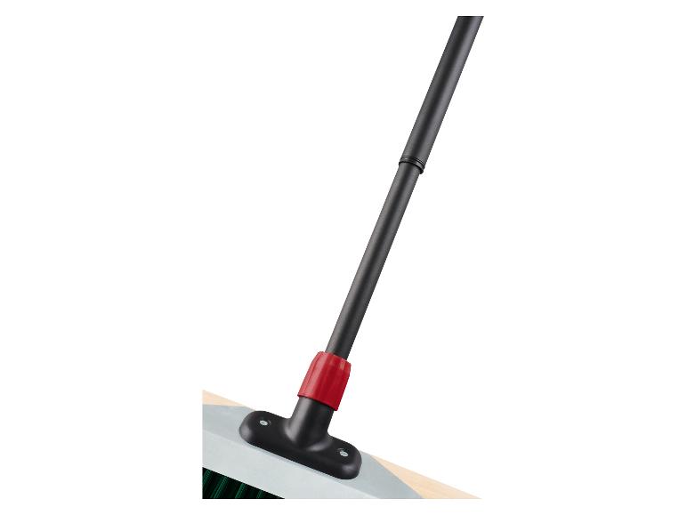 Gros plan d'un balai avec un manche noir et un connecteur rouge, fixé à une base claire.