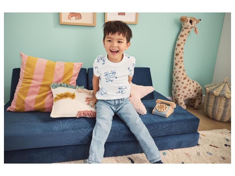 Un garçon souriant est assis sur un canapé modulaire bleu avec des coussins décoratifs et une girafe en peluche.