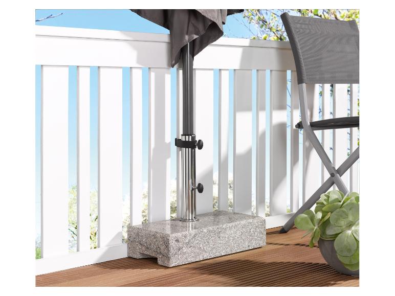 Base de parasol en granit sur une terrasse en bois avec une chaise et une plante.