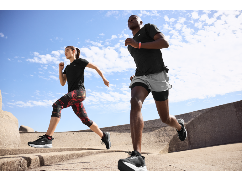 Deux personnes courent en extérieur en tenue de sport noire, incluant t-shirts, shorts et leggings.