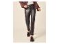 Personne portant un pantalon en faux cuir marron foncé, un pull clair et une veste marron.