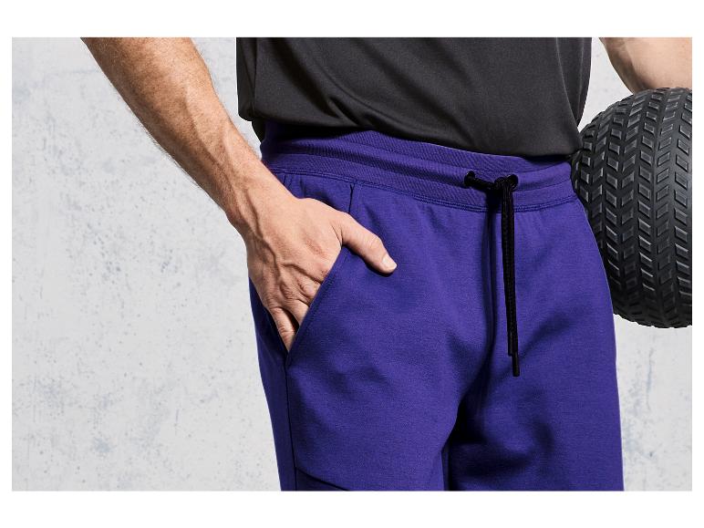 Homme avec un pantalon de survêtement violet et un ballon de fitness noir.