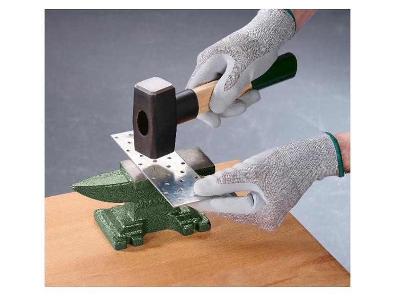 Mains gantées martelant une plaque métallique sur une enclume.