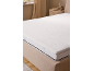 Surmatelas blanc sur un lit dans une chambre aux tons neutres.