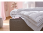 Couette blanche pliée avec liseré bleu sur un lit beige dans une chambre.