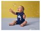 Bébé en t-shirt requin bleu jouant avec des bulles de savon sur fond jaune.