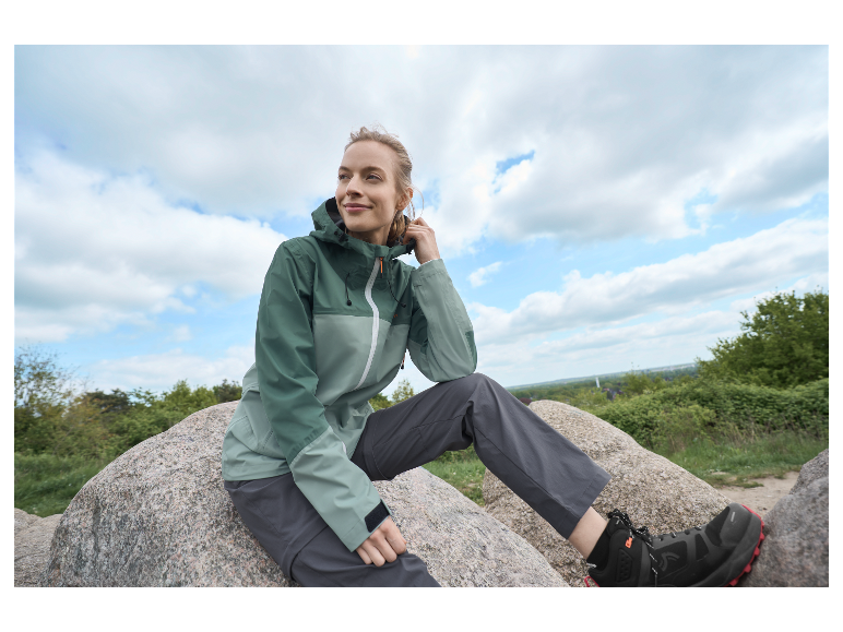 Femme assise sur un rocher, vêtue d'une veste et d'un pantalon de sport.
