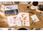 Ensemble de crayons aquarelle dans une boîte métallique sur un bureau en bois avec des dessins de fleurs.