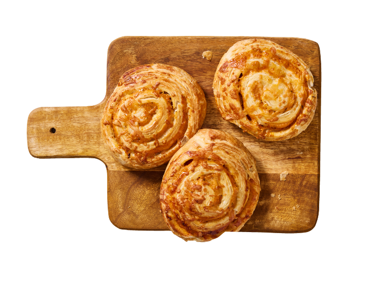 Trois escargots à la cannelle sur une planche à découper en bois.