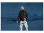 Un homme portant une veste noire Mountain Warehouse et un pantalon blanc devant un paysage montagneux.