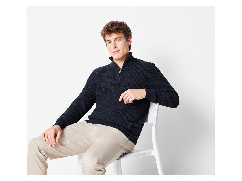 Un homme portant un pull bleu marine à fermeture éclair et un pantalon beige.