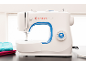 Machine à coudre blanche avec accent bleu et pile de tissu sur une table sombre.
