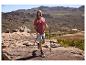 Homme en t-shirt et short de randonnée, avec bâtons de trekking, dans un paysage montagneux.