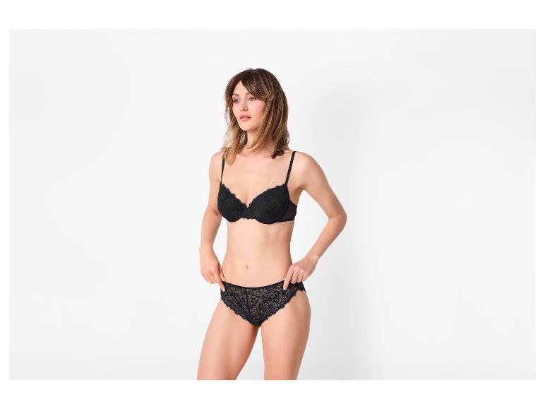 Femme en soutien-gorge et culotte en dentelle noire, posant sur fond blanc.