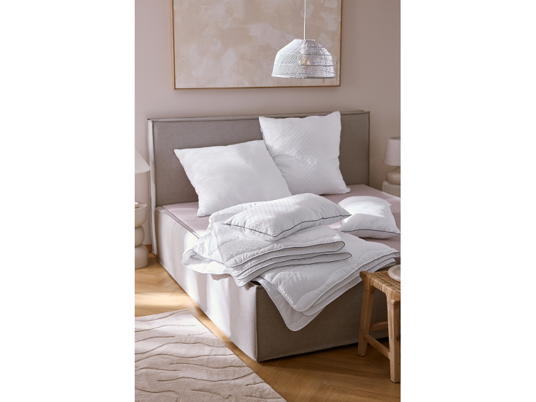 Parure de lit blanche avec oreillers et couettes sur un lit dans une chambre aux tons neutres.