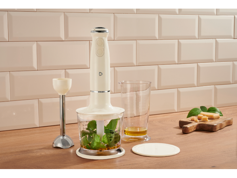 Mixeur plongeant crème avec herbes, huile et fromage sur une surface en bois.