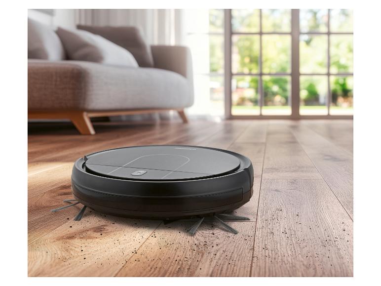 Aspirateur robot sur un parquet avec de la saleté, dans un salon.