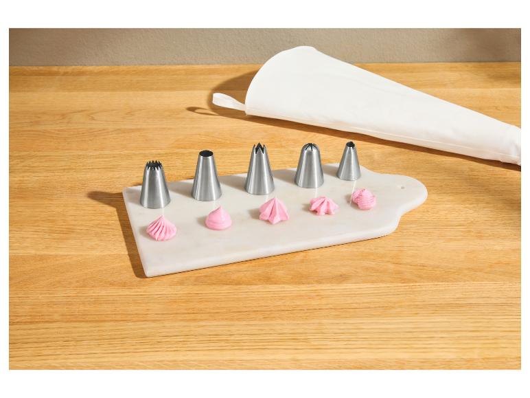 Ensemble de douilles de pâtisserie avec glaçage rose sur une planche en marbre et une poche à douille.