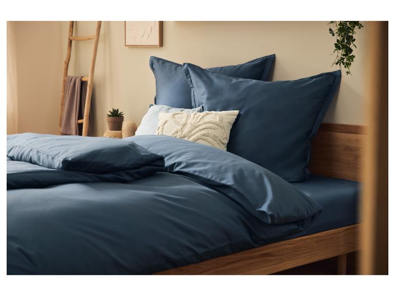 Parure de lit bleu marine sur un lit en bois avec coussins décoratifs et plantes.