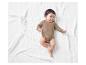 Bébé dans un body beige allongé sur une couverture blanche.