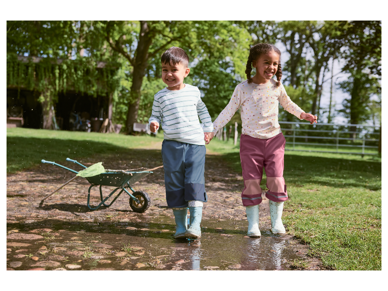 Deux enfants heureux en bottes de pluie jouent dans une flaque d'eau.