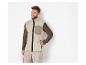 Un homme porte un gilet en polaire beige avec un pull marron dessous.