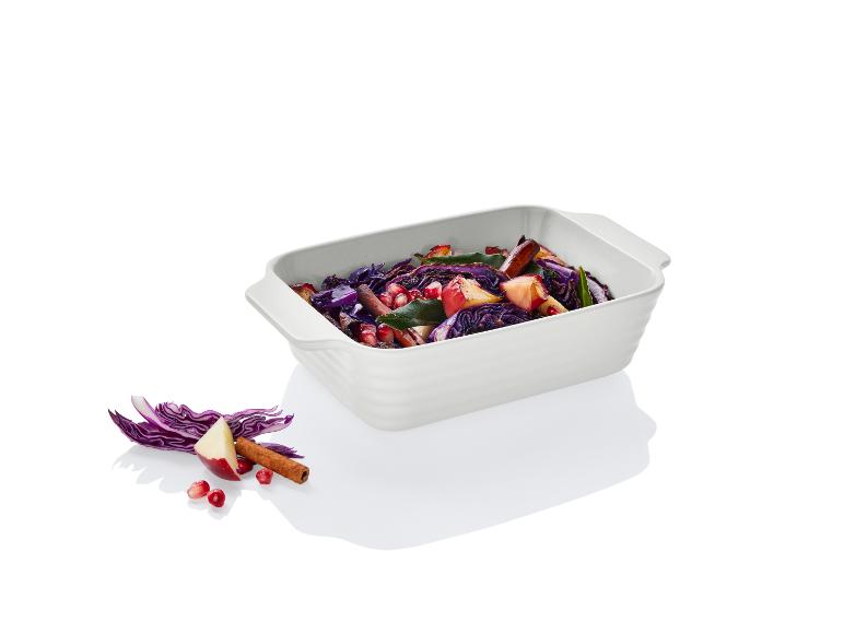 Un plat blanc avec du chou rouge, une pomme et une grenade.