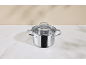 Casserole en acier inoxydable avec couvercle en verre sur un comptoir en marbre blanc.